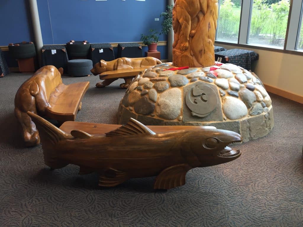 Benches by "We Are Here" wood carving at SOU library.