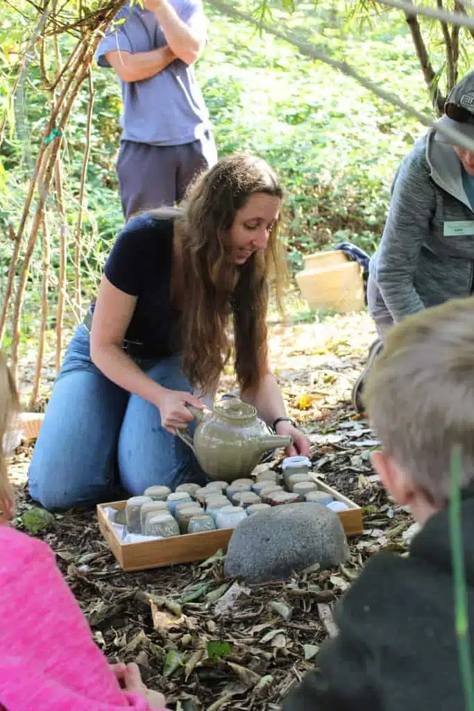 Libby is making manzanita tea with a school group inside the Living Willow Hut.
