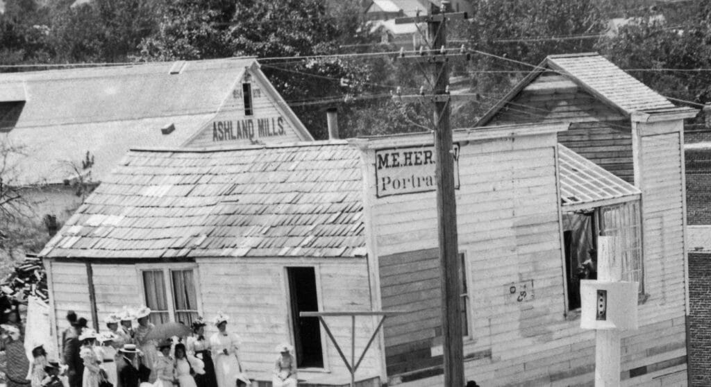 1898 Ashland 4th of July parade photo. Close-up of M.E. Herrin Portrait photographer building and Ashland Flour Mill behind it.