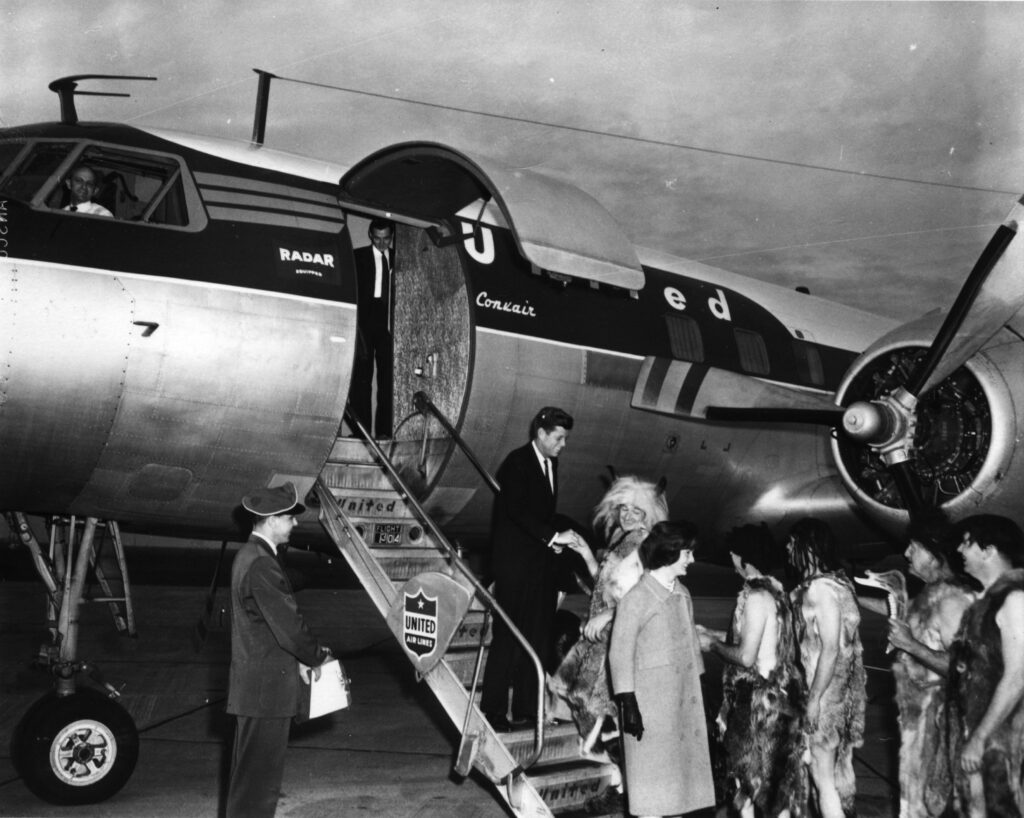 Senator and Jacqueline Kennedy arrive at Medford airport, March 6, 1959. Grants Pass Cavemen greet them at plane. (photo SOHS #14066)