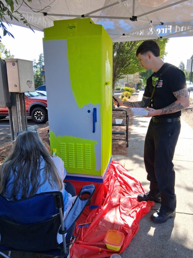 Fire Department staff Jacob ? putting base coat of caution yellow on the "fire station" traffic signal box.