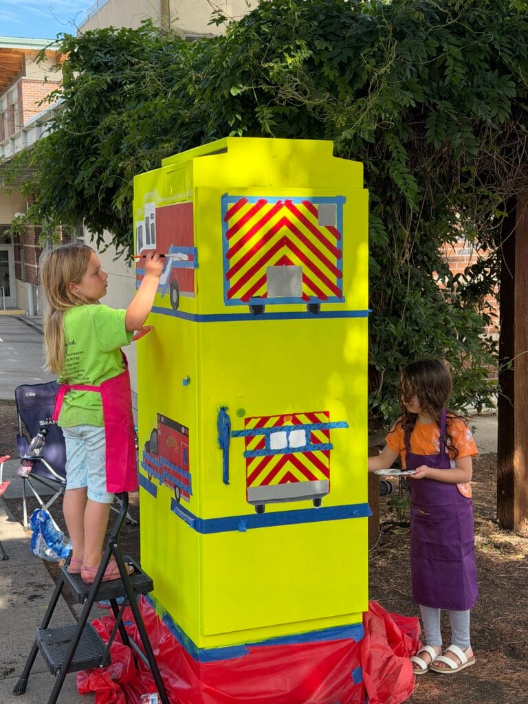 Two of artist Glory Nylander's children are painting the traffic signal box: "Fire Engine and Ambulance."