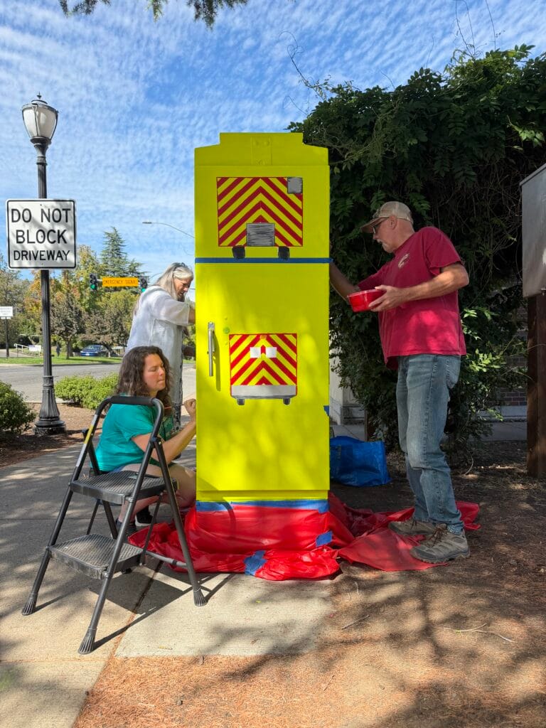Glory, her mother Lorrie and step-father David are painting the traffic signal box: "Fire Engine and Ambulance."